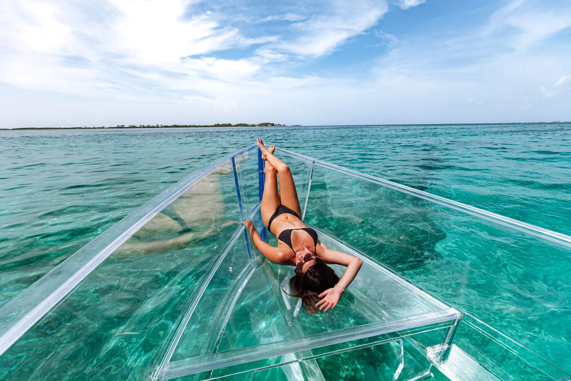 A guest relaxing at the bow of a clear boat on turquoise water